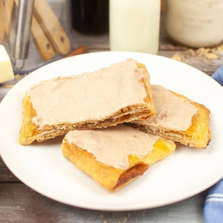 Three pop tarts with brown sugar and cinnamon filling topped with powdered sugar and cinnamon icing on a plate.