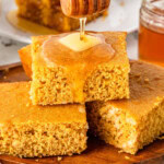 Slices of sweet cornbreads sitting on a wooden plate drizzled with honey.