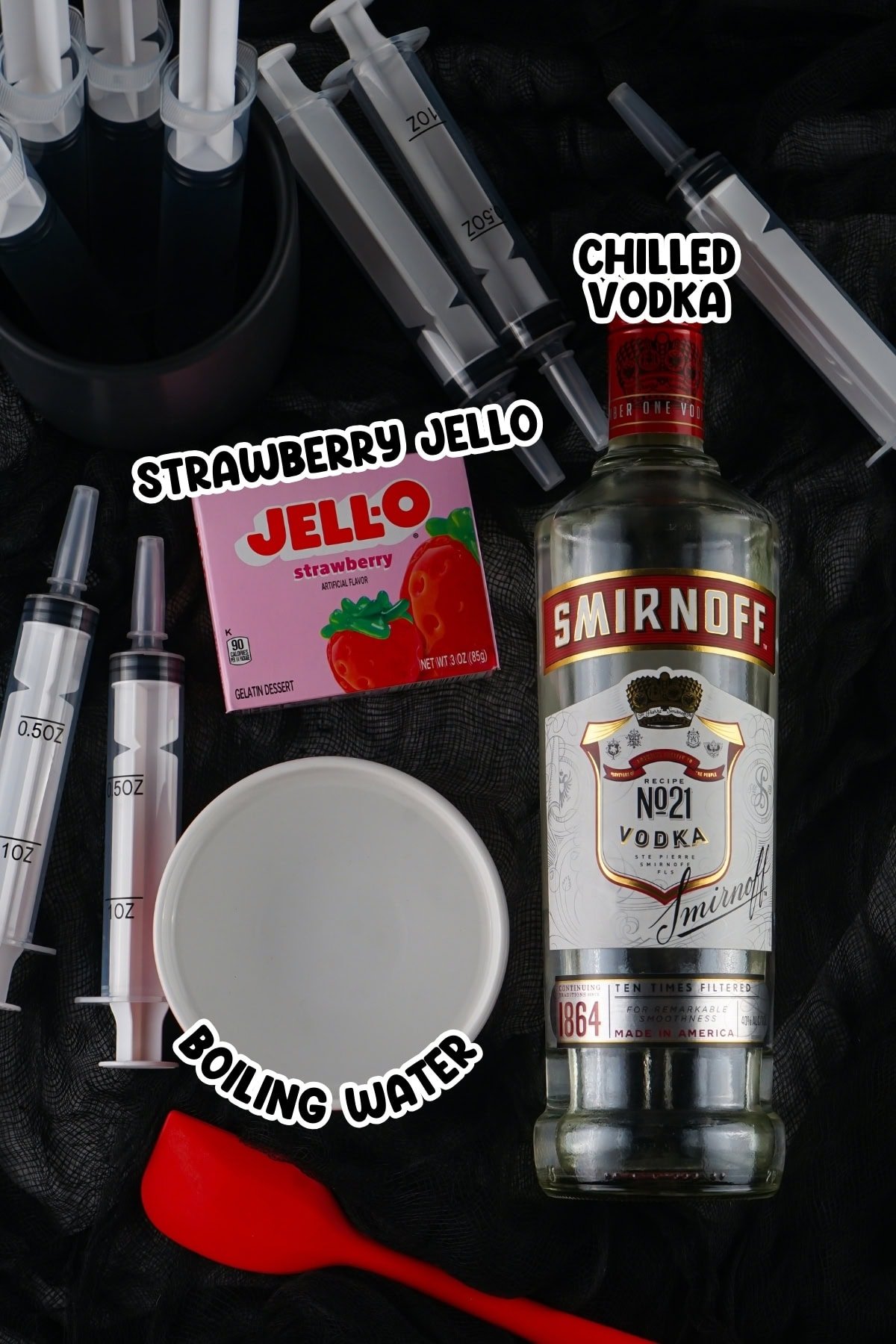 Ingredients for red jello shots sitting on a black mesh cloth.