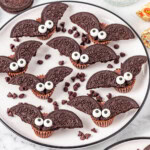 A white plate with Reese's chocolate topped with Oreo half into two pieces added with candy eyes to look like a bat.