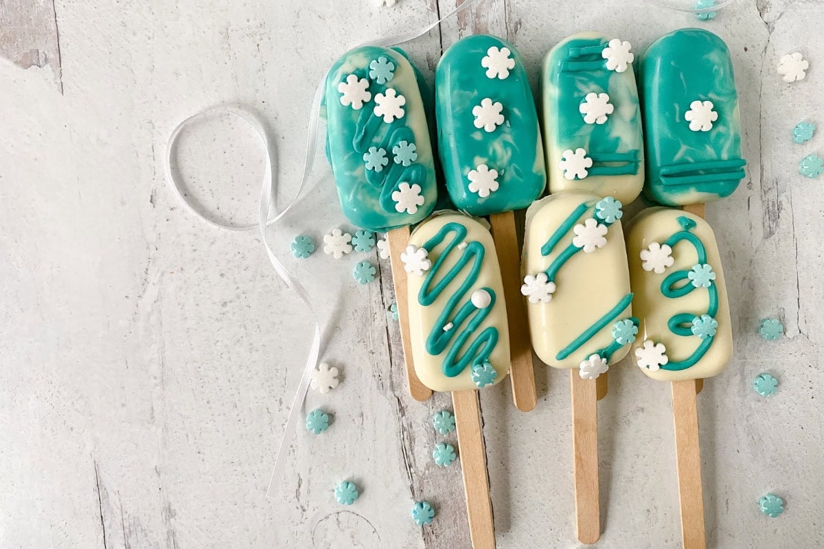 Winter wonderland themed cake pops sitting on a white wooden table.