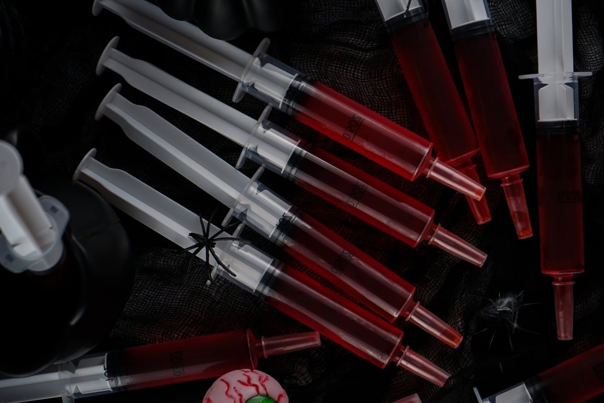 Red jello shots in syringes sitting on a black mesh cloth.