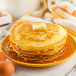 A stack of pancakes with a pat of butter on top, served on a yellow plate.