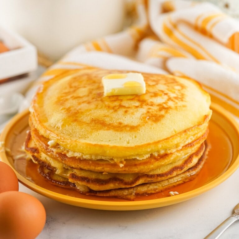 A stack of pancakes with a pat of butter on top, served on a yellow plate.