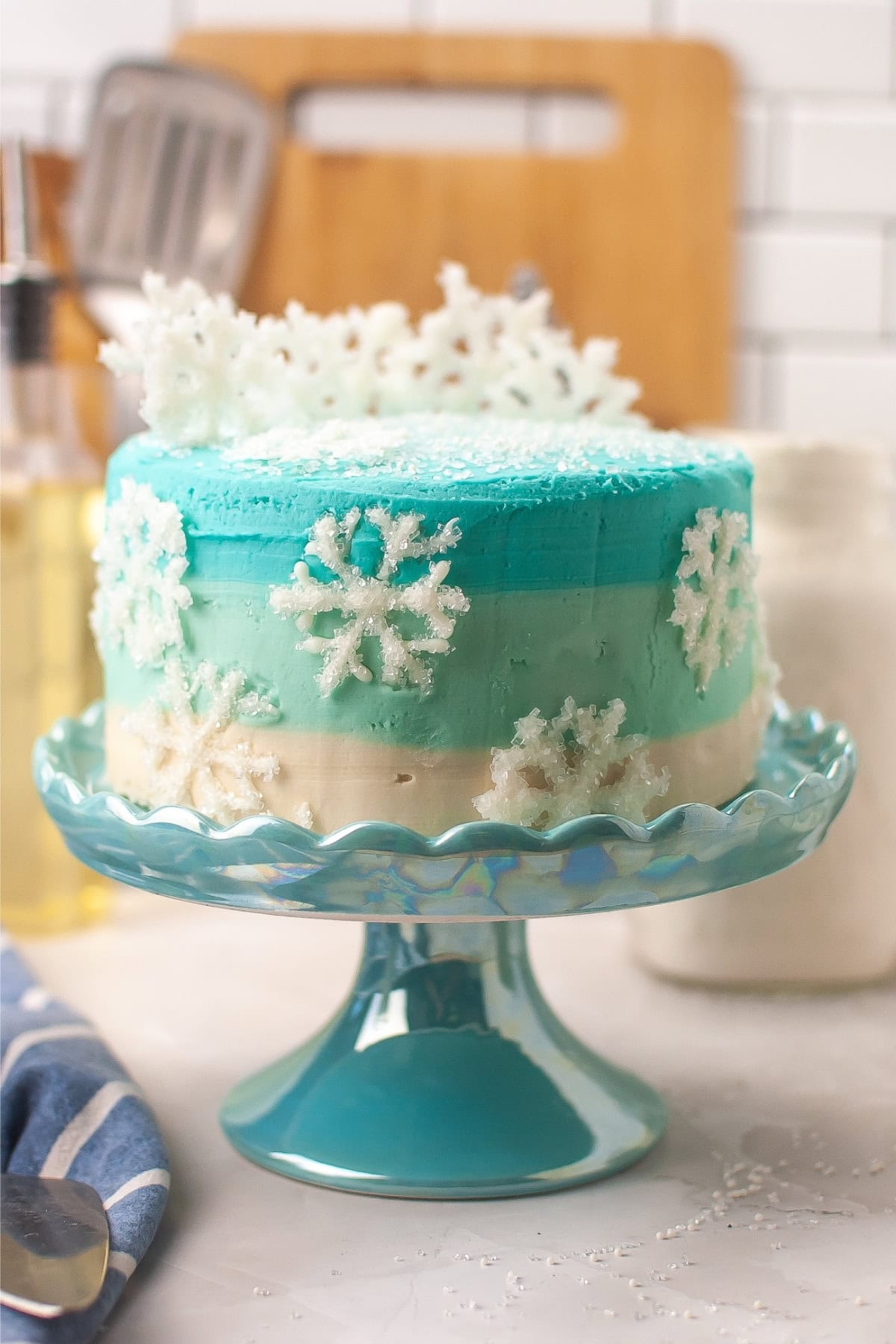 A blue and white cake with snowflake decorations on a glass cake stand.
