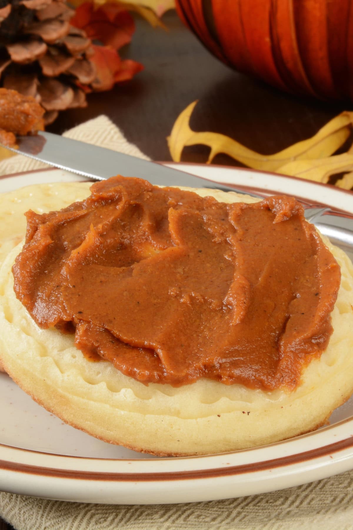 A waffle topped with spiced pumpkin butter on a plate, with a knife and autumn leaves in the background.