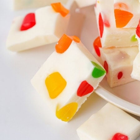 A nougat cut into squares with colorful Dots candy pieces on a plate, scattered on a white surface.