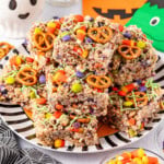 A plate of Halloween-themed rice crispy treats topped with pretzels, candy corn, and colorful candies.