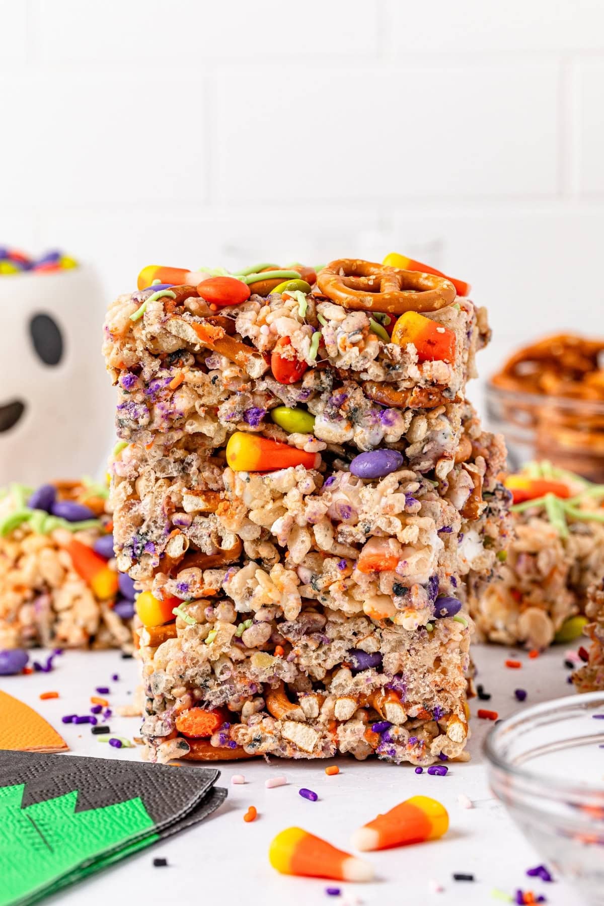Stacked rice crispy treats with colorful candies and pretzels on top, surrounded by candy corn and sprinkles.