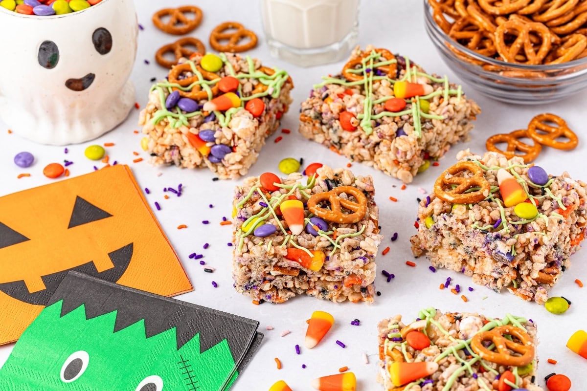 Halloween-themed rice crispy treats with candy decorations, surrounded by pretzels and festive napkins.
