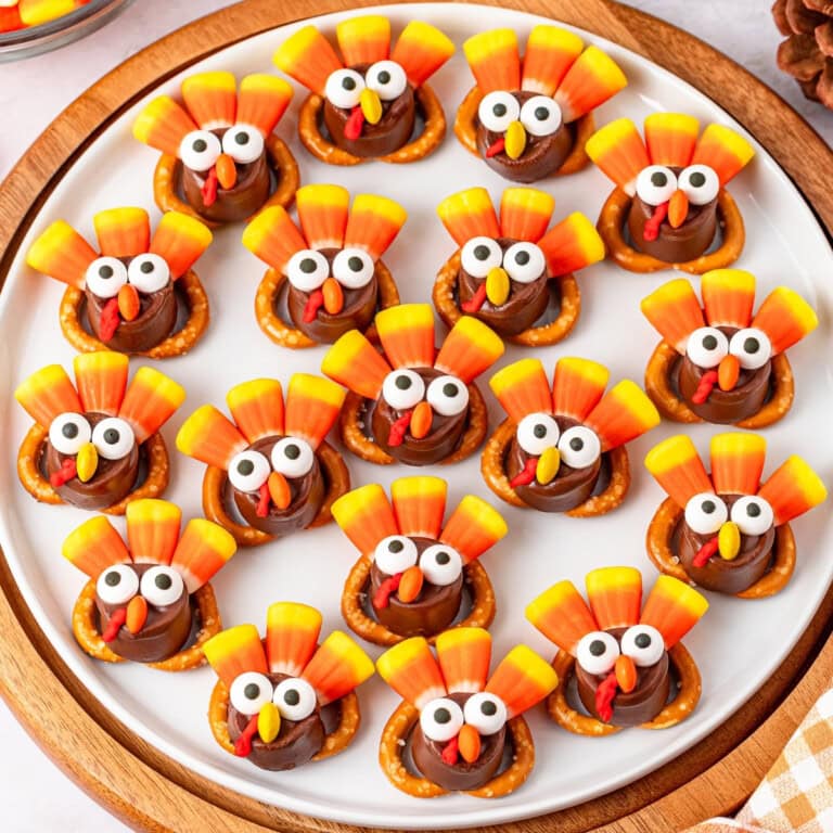 A platter of turkey-shaped treats with candy corn tails and pretzel bases arranged neatly on a circular white plate.