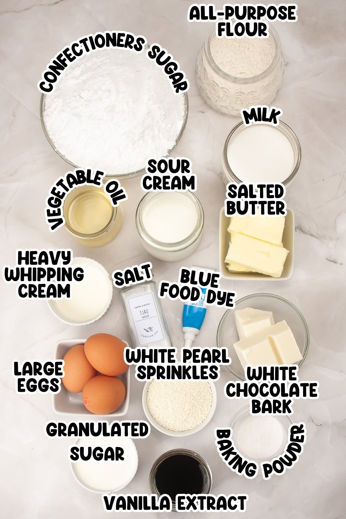 Ingredients for baking, including flour, sugar, eggs, butter, milk, sour cream, and more, with labels on a marble surface.