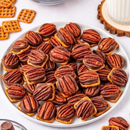 A white plate of pretzel topped with pecan, and rolo chocolate snacks.