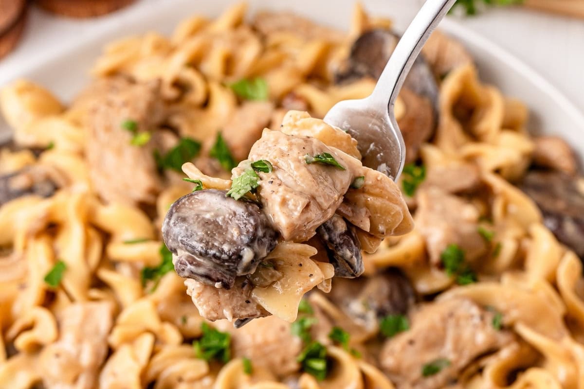Creamy mushroom pasta on a fork, garnished with herbs.
