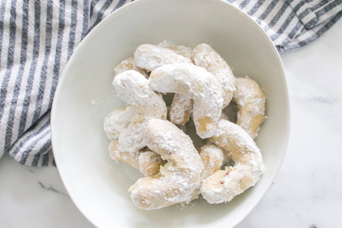 Powdered sugar crescent cookies in a white bowl.