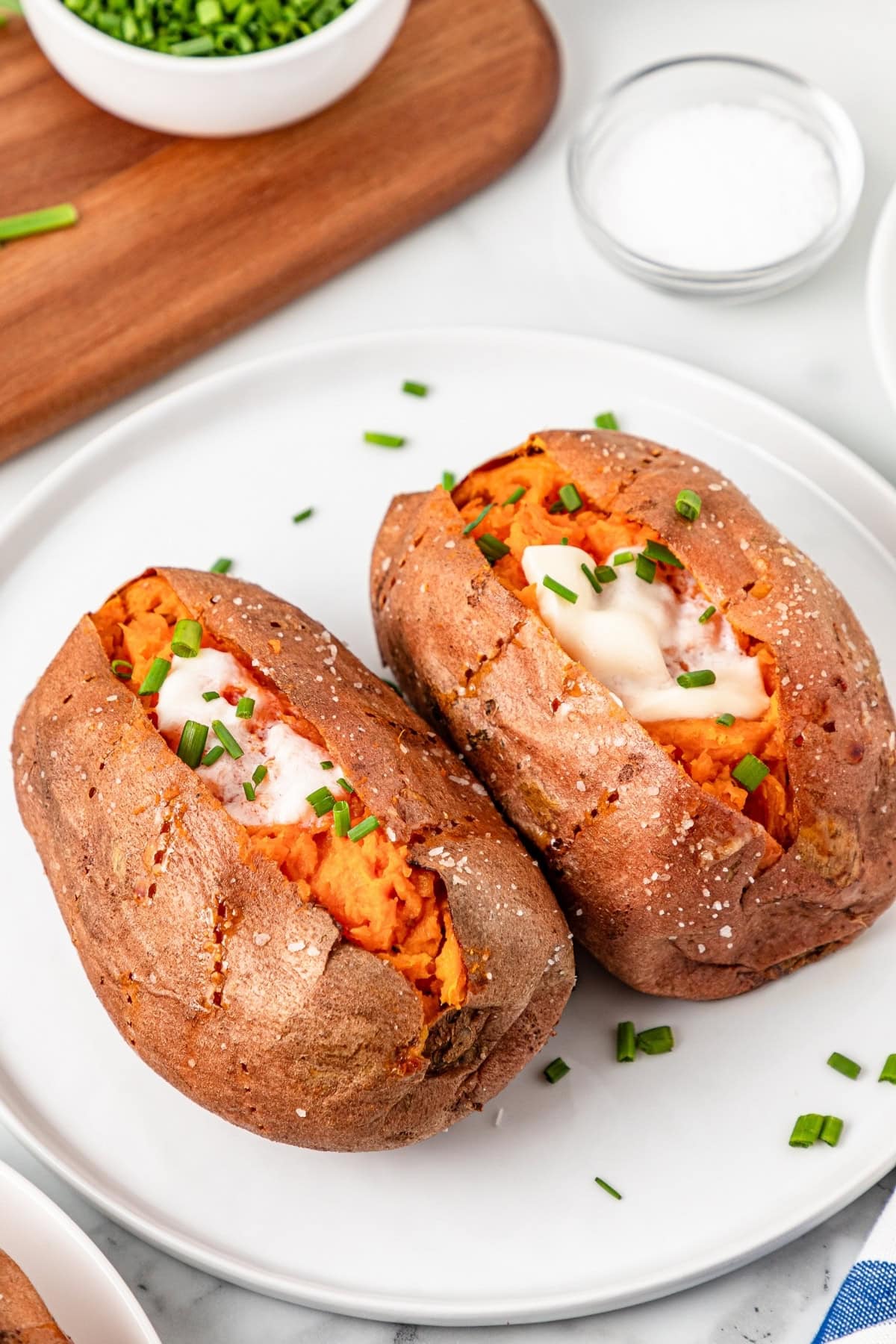 Two baked sweet potatoes with butter and chives on a white plate.