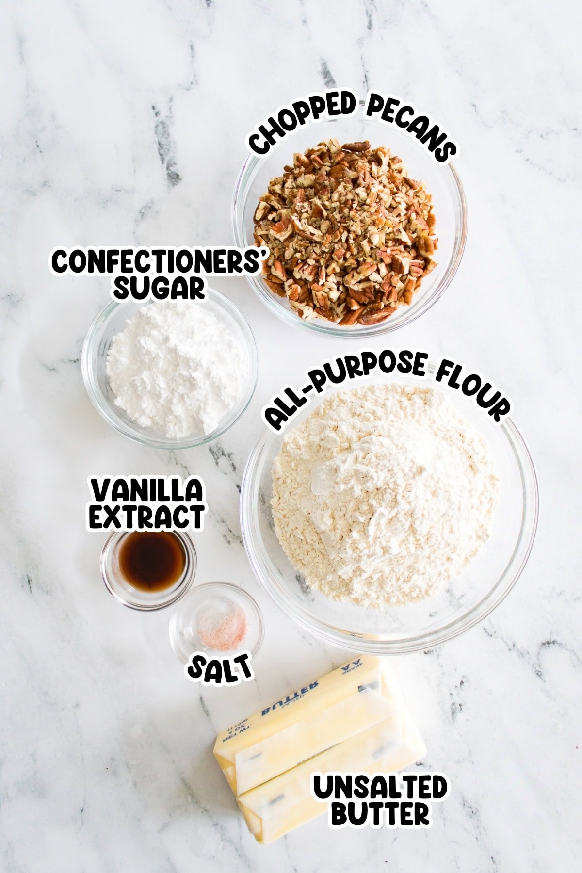 Baking ingredients on a marble surface: pecans, flour, sugar, vanilla, salt, butter.