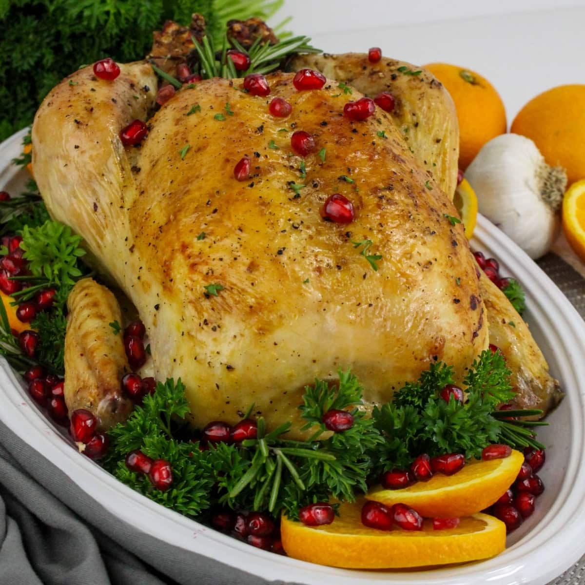 Roasted chicken garnished with herbs, pomegranate seeds, and orange slices.