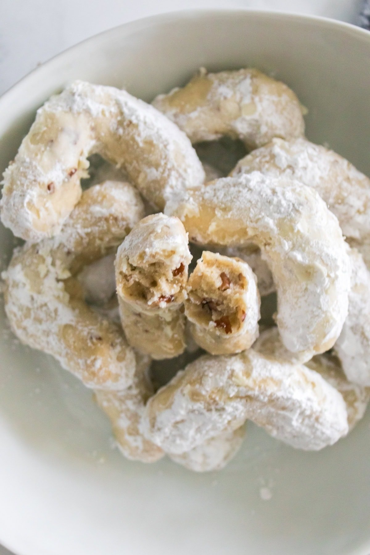 Powdered sugar crescent cookies piled in a bowl.