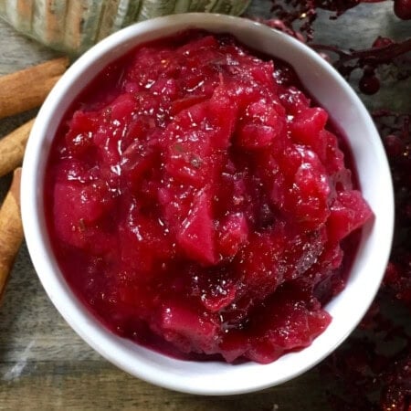 A bowl of red cranberry sauce on a wooden table.
