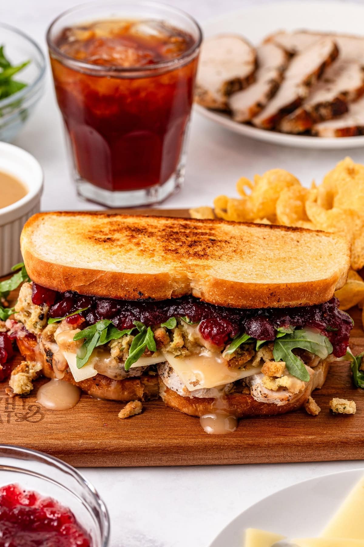 Gourmet sandwich with turkey, cranberry sauce, and a side of chips and iced tea.