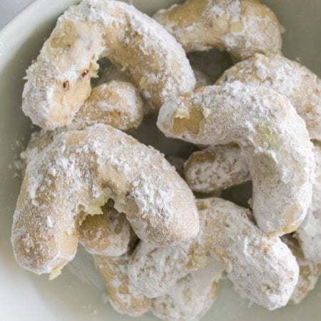 Crescent cookies with powdered sugar piled in a white bowl.