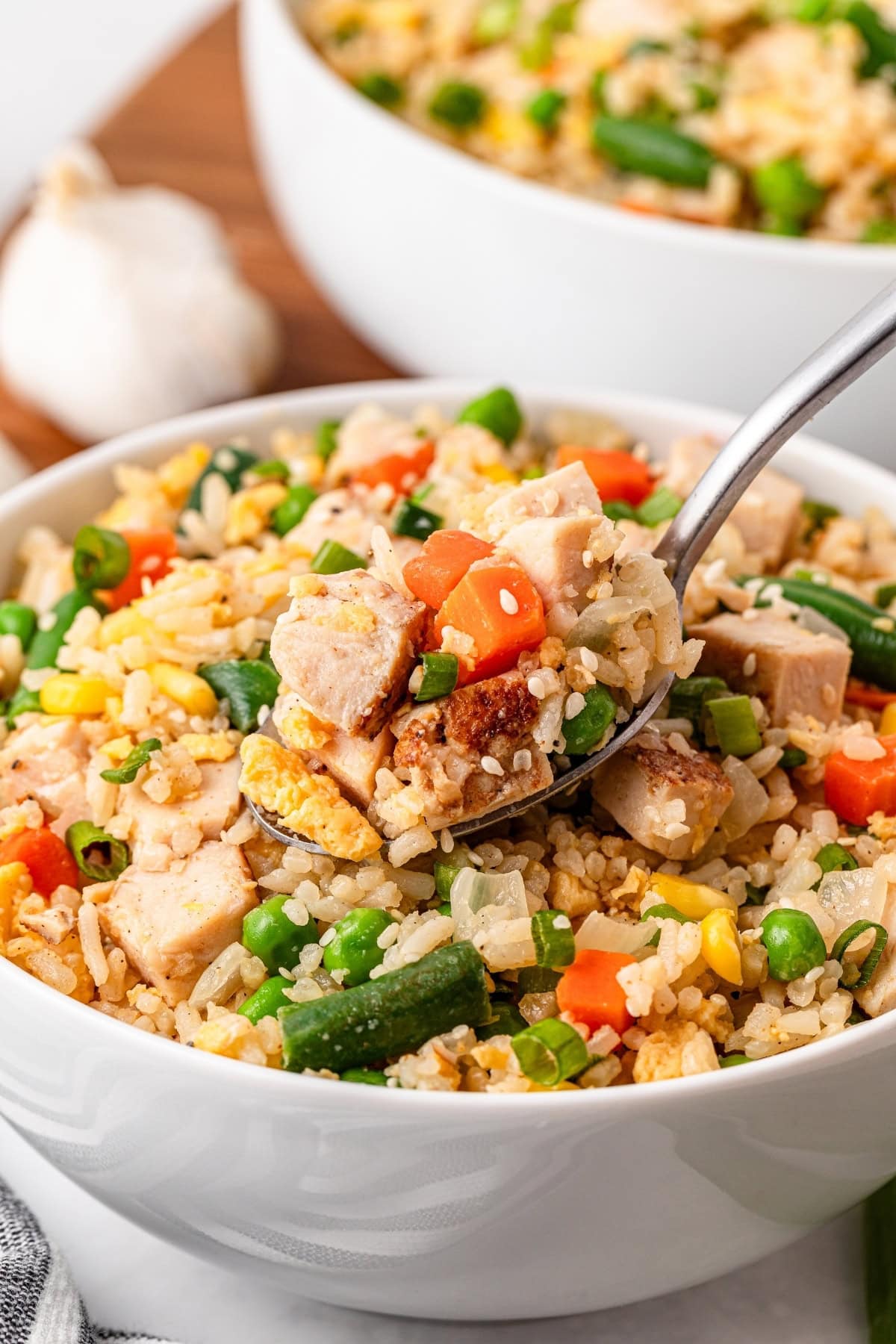 Bowl of chicken fried rice with vegetables and a spoon.