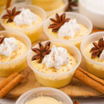 Small cups of Eggnog Pudding Shots with whipped cream and star anise garnish.