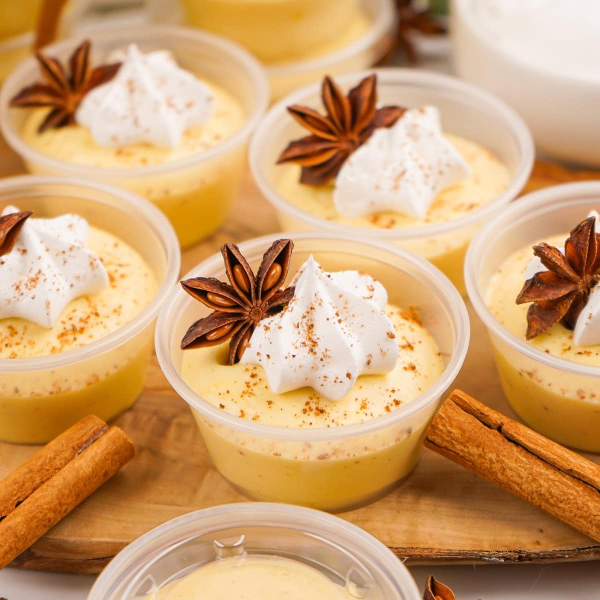 Small cups of Eggnog Pudding Shots with whipped cream and star anise garnish.