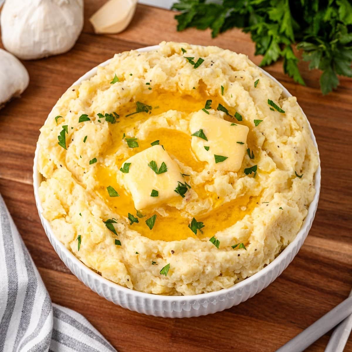 Mashed potatoes with butter and parsley in a white bowl on a wooden surface.