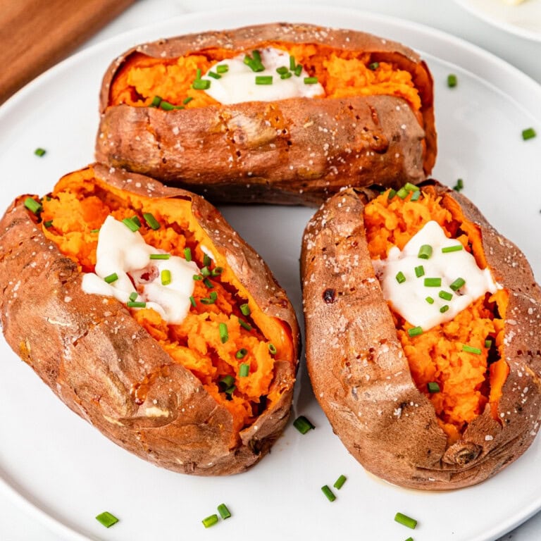 Three baked sweet potatoes topped with butter and chives on a plate.