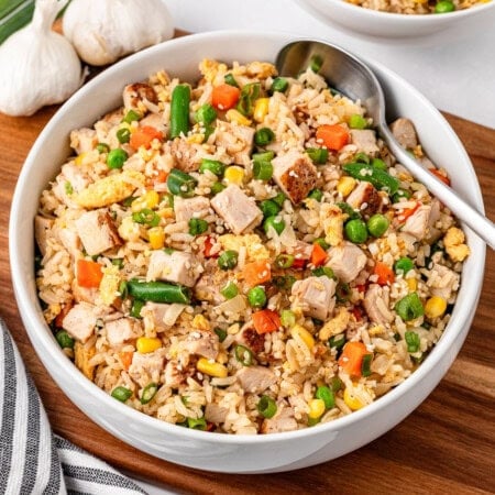 Bowl of fried rice with vegetables and chicken, served with a spoon.