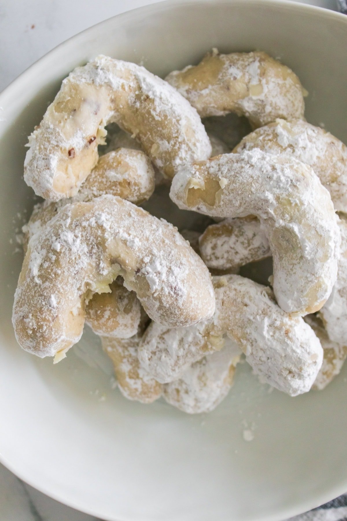 Crescent cookies with powdered sugar in a white bowl.