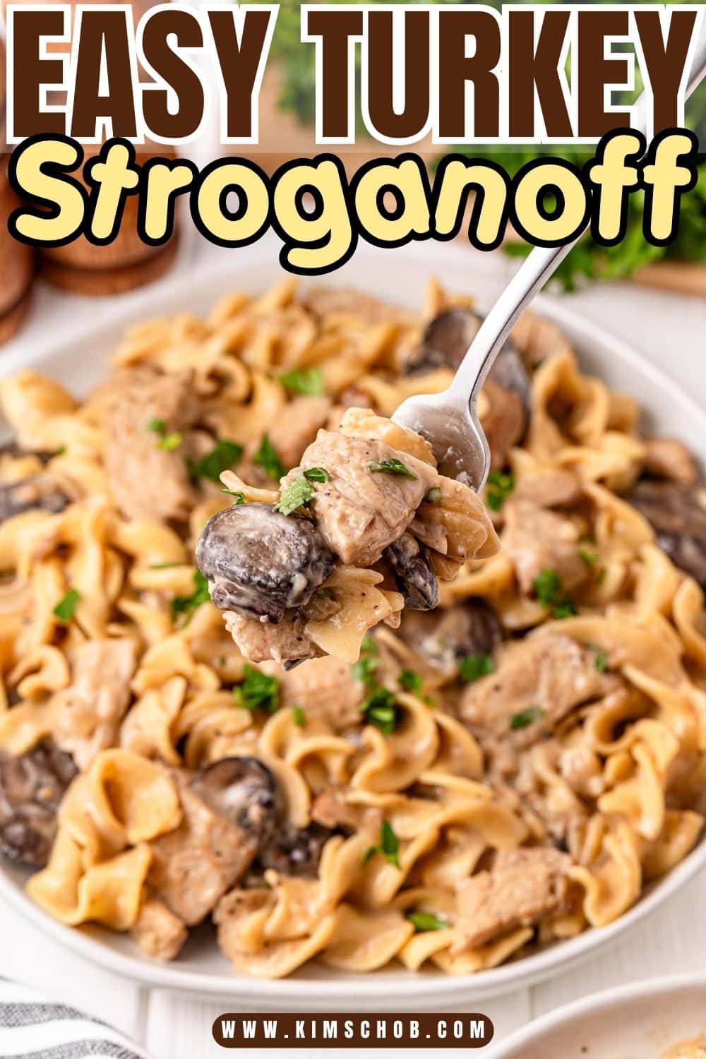 A spoonful of turkey stroganoff above a plate of noodles and mushrooms.
