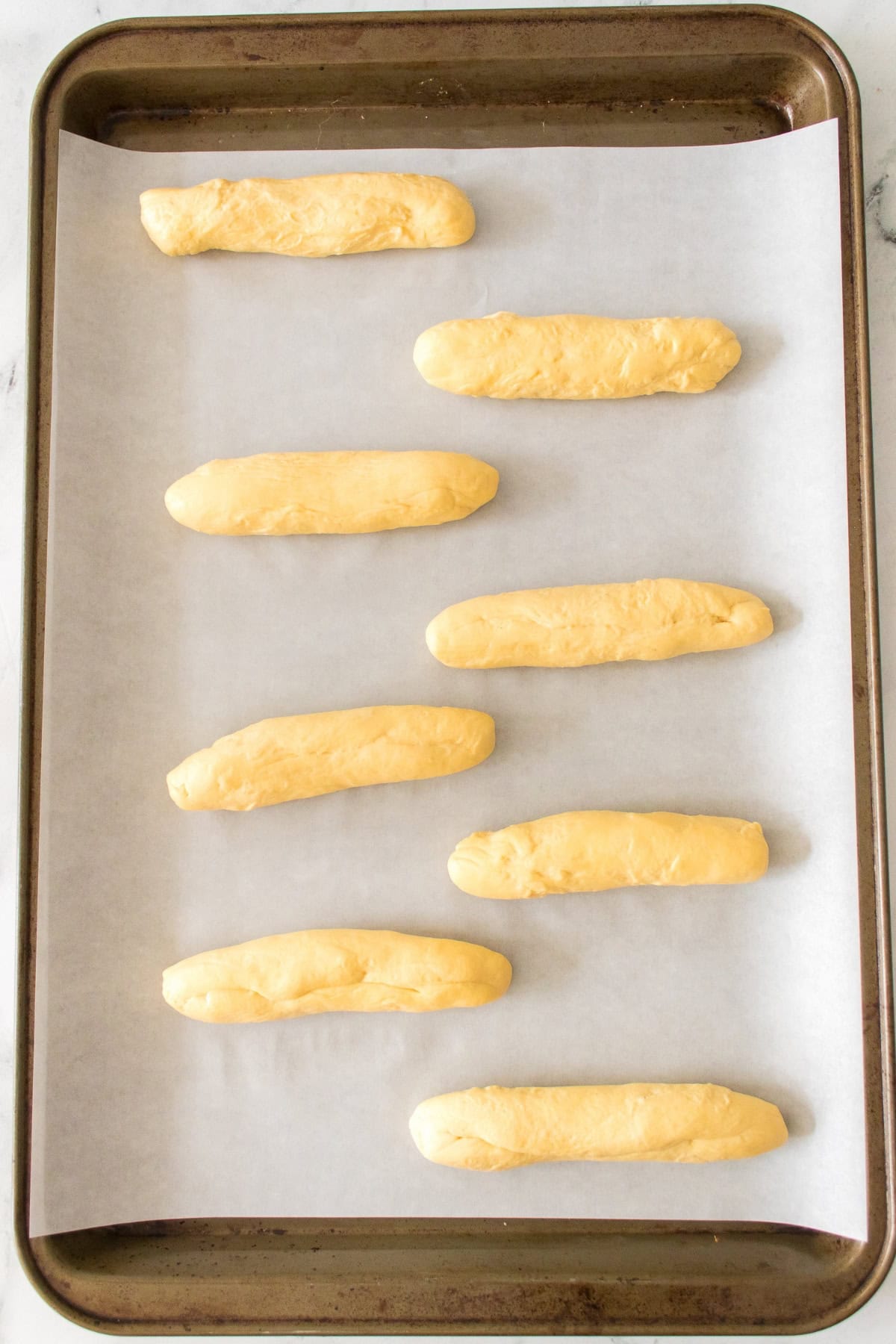 Eight unbaked breadsticks on a parchment-lined baking sheet.