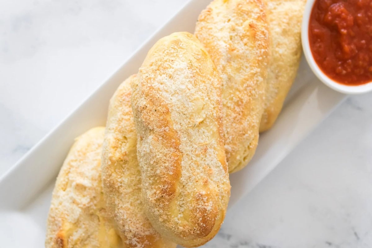 Breadsticks with cheese on a plate, served with marinara sauce.
