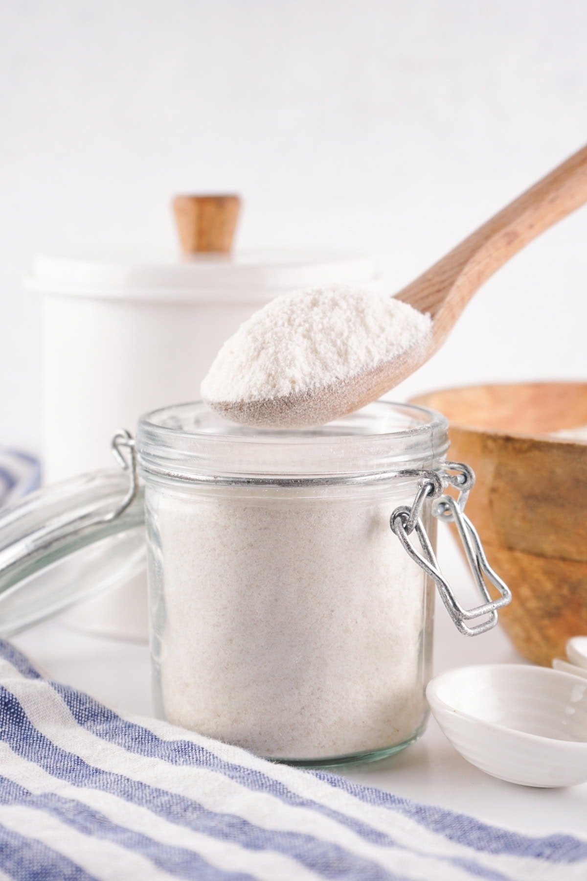 Wooden spoon lifting flour over a glass jar with a lid.