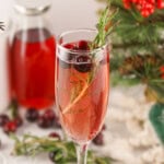 Mimosa with cranberries and rosemary garnish in a champagne flute.