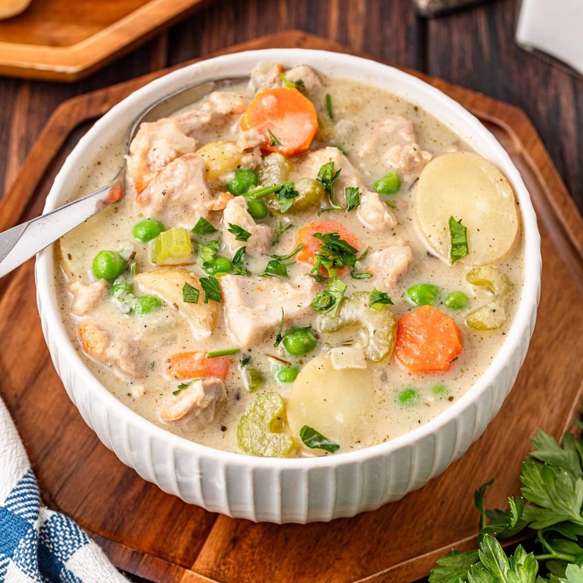 Creamy chicken stew with vegetables in a white bowl on a wooden board.