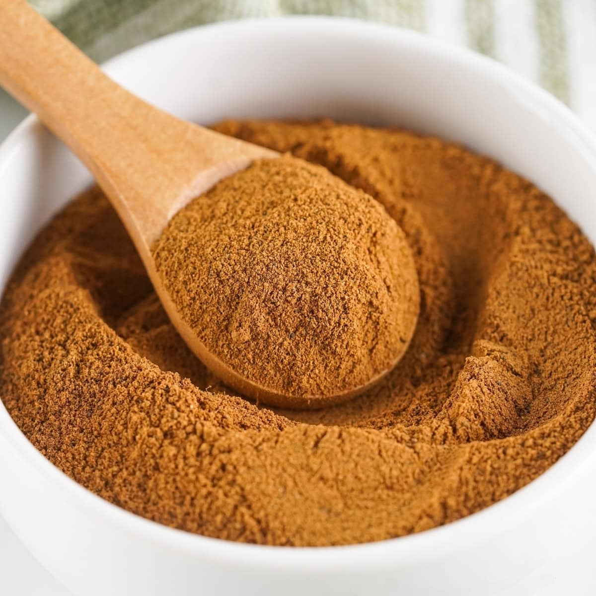 Wooden spoon in a white bowl of spice blend.
