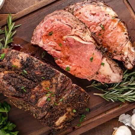 Sliced roast beef on a wooden board with rosemary and garlic.