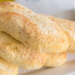 Golden breadsticks topped with cheese on a white plate.