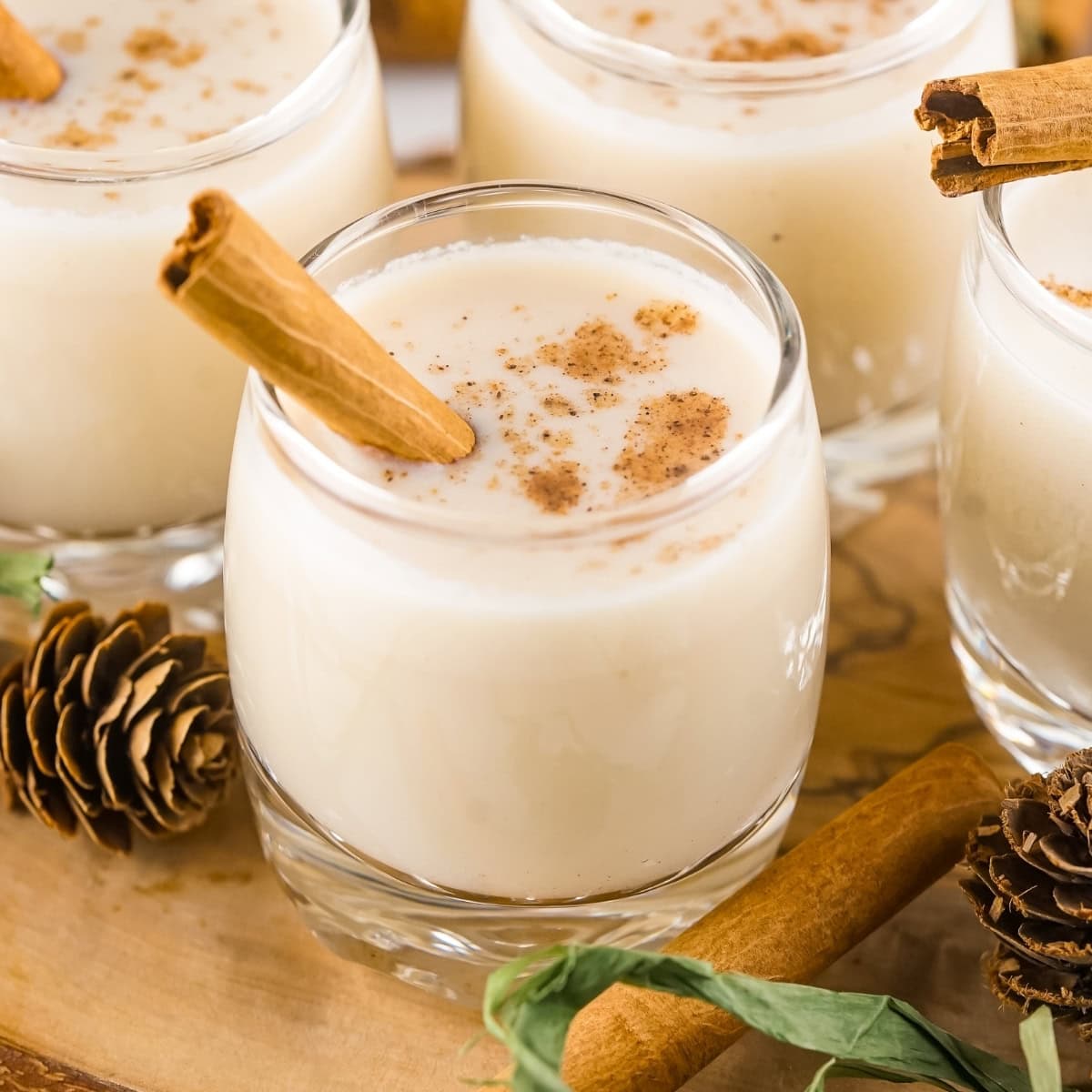 Creamy eggnog in glasses with cinnamon sticks and sprinkled nutmeg.