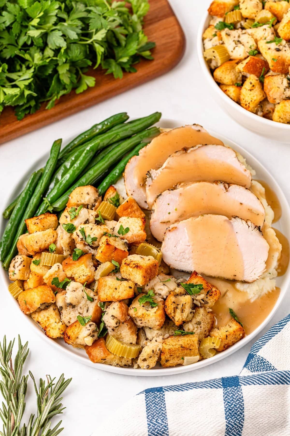 Plate of turkey slices with gravy, stuffing, green beans, and herbs.