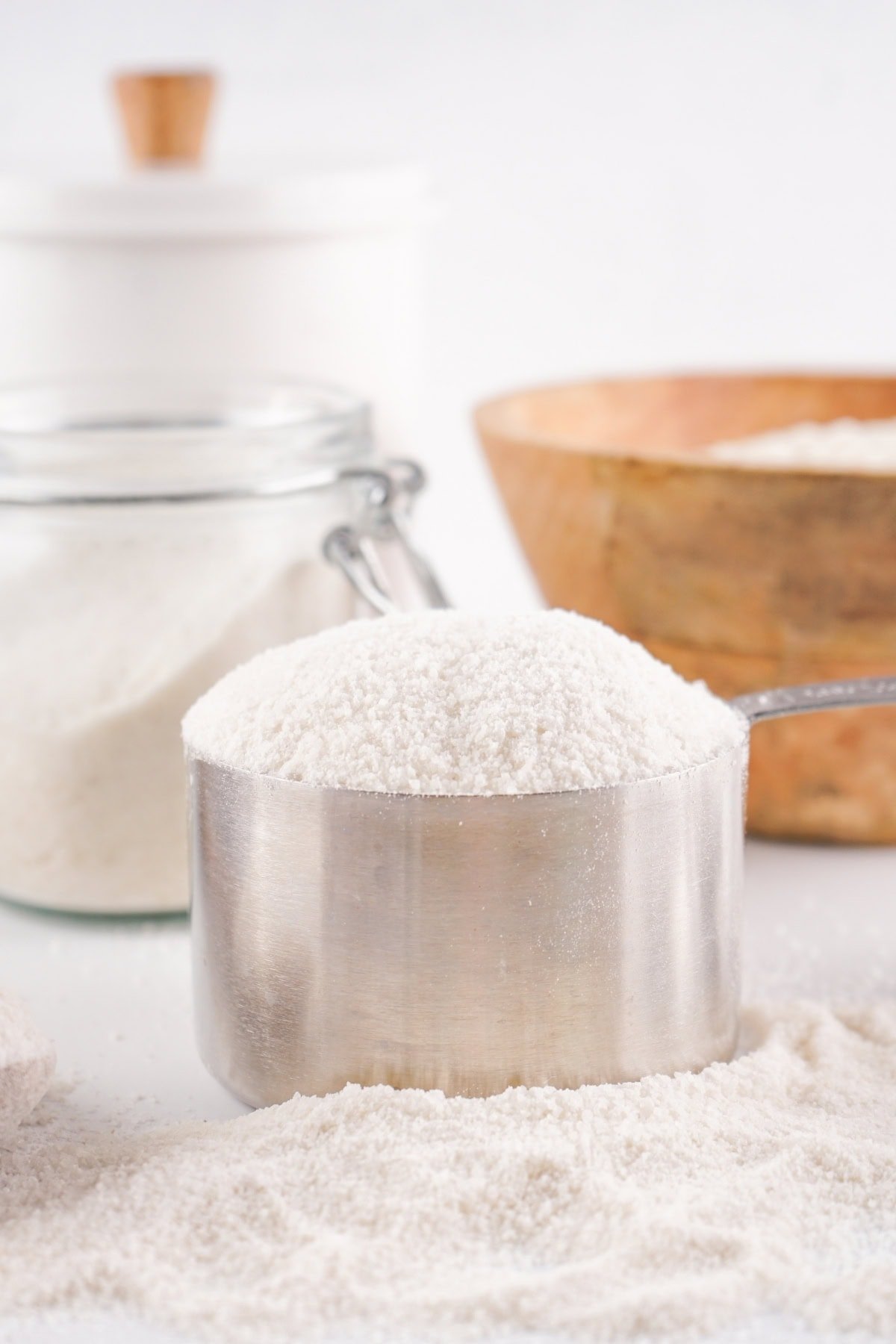 A metal measuring cup filled with flour on a white surface.
