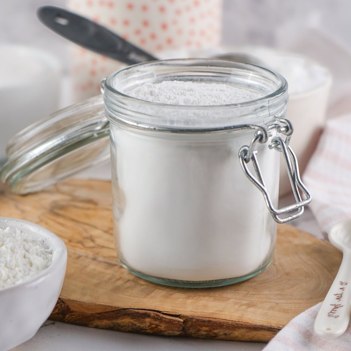 A glass jar of homemade powdered sugar on a wooden board, with a spoon inside.