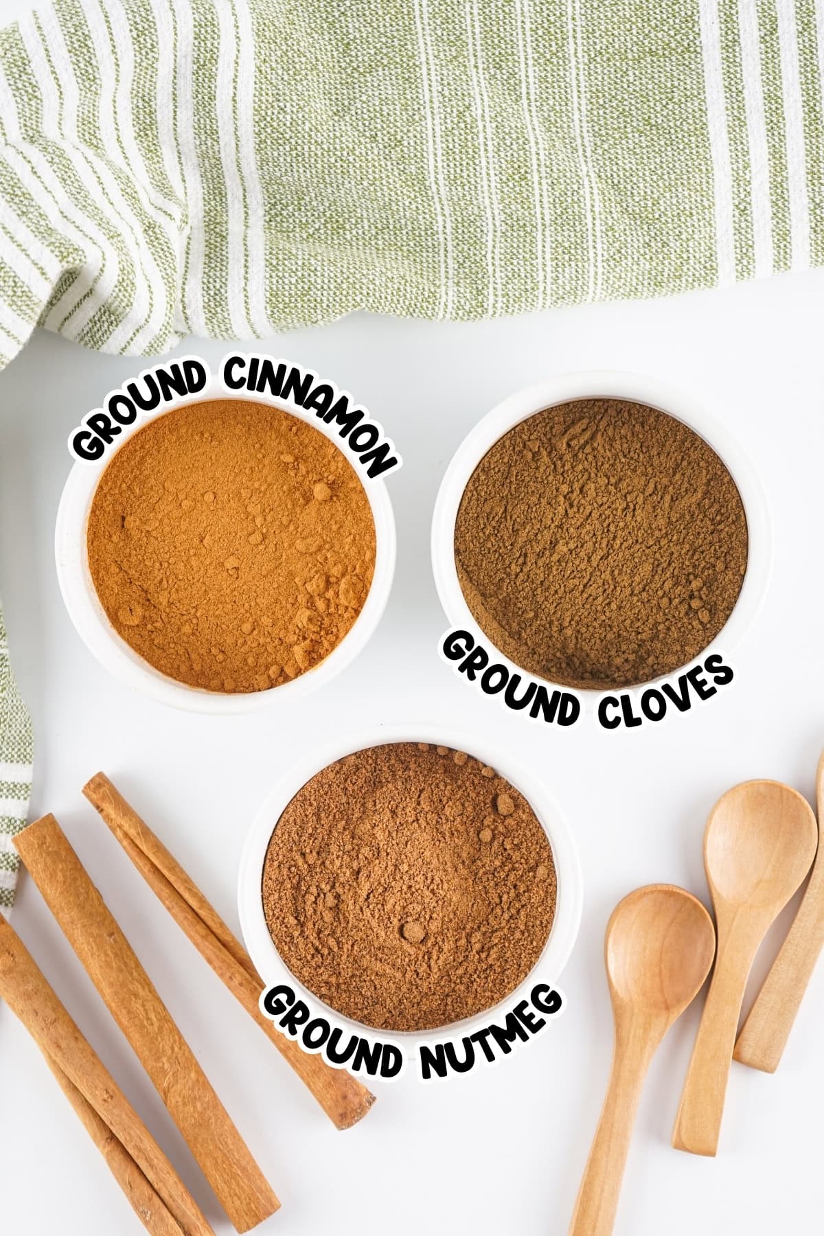 Three bowls of ground spices with labels: cinnamon, cloves, nutmeg; wooden spoons.
