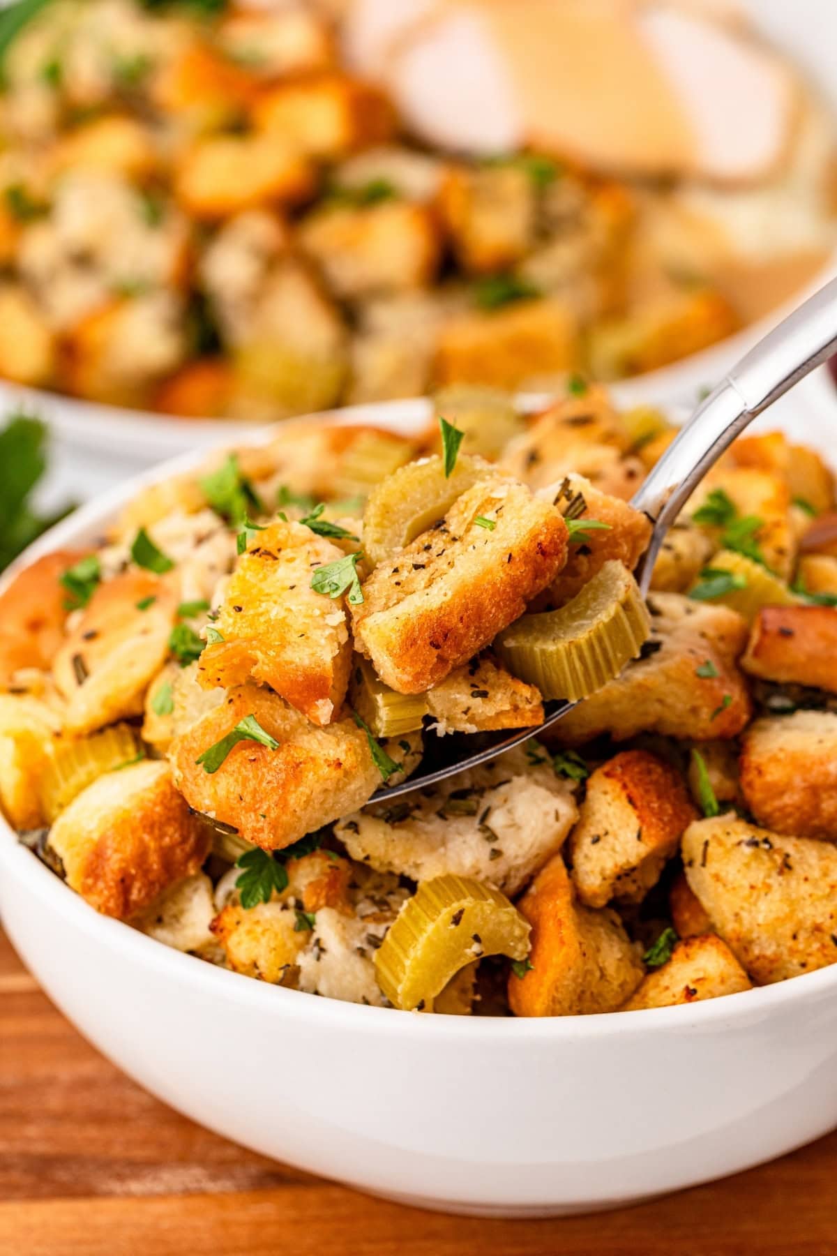 Bowl of stuffing with bread cubes and celery being served with a spoon.