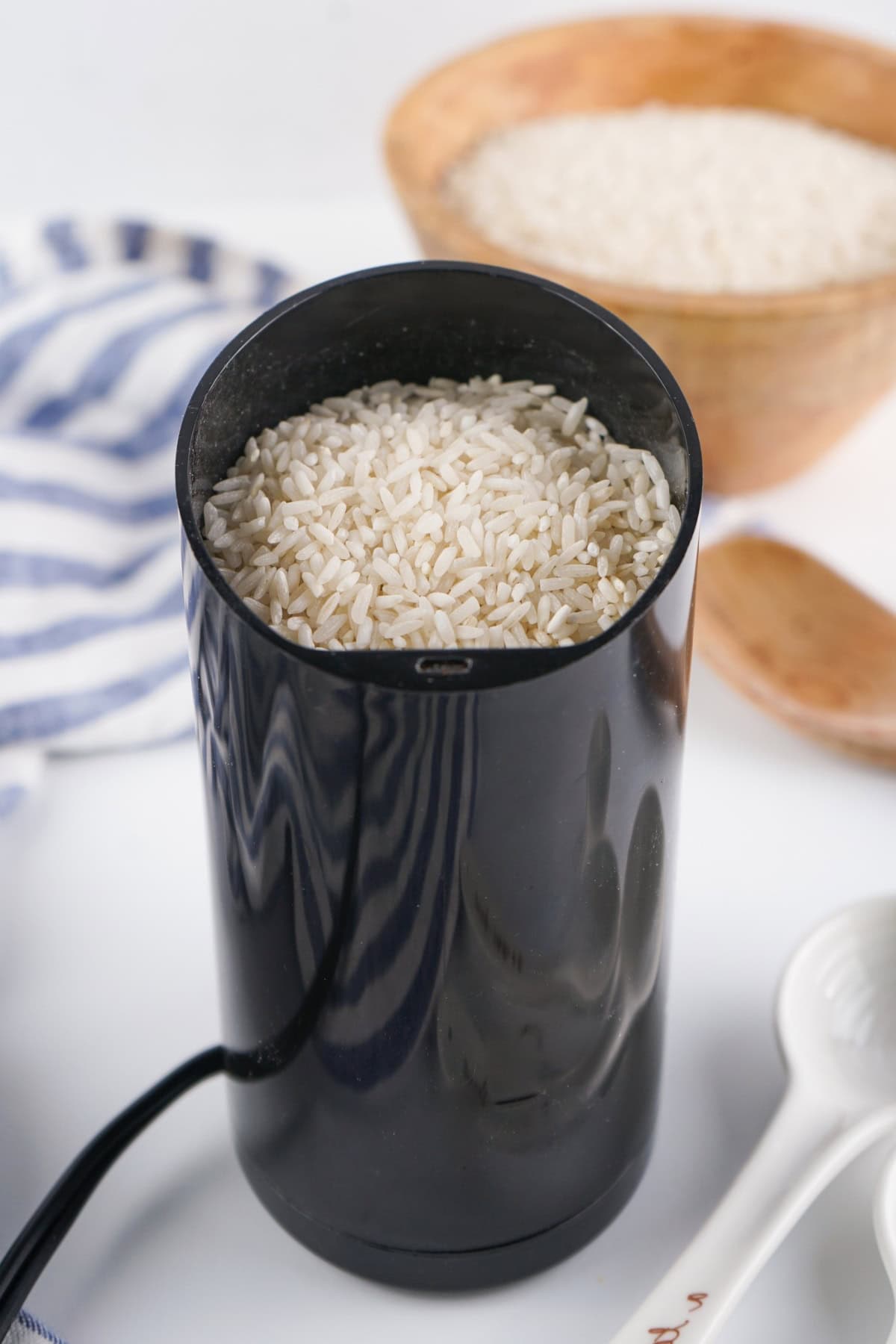 Black electric grinder filled with uncooked rice.