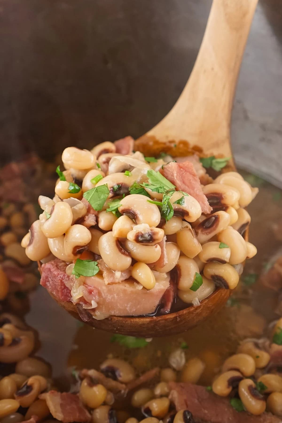 Ladle of black-eyed peas with ham and chopped herbs.